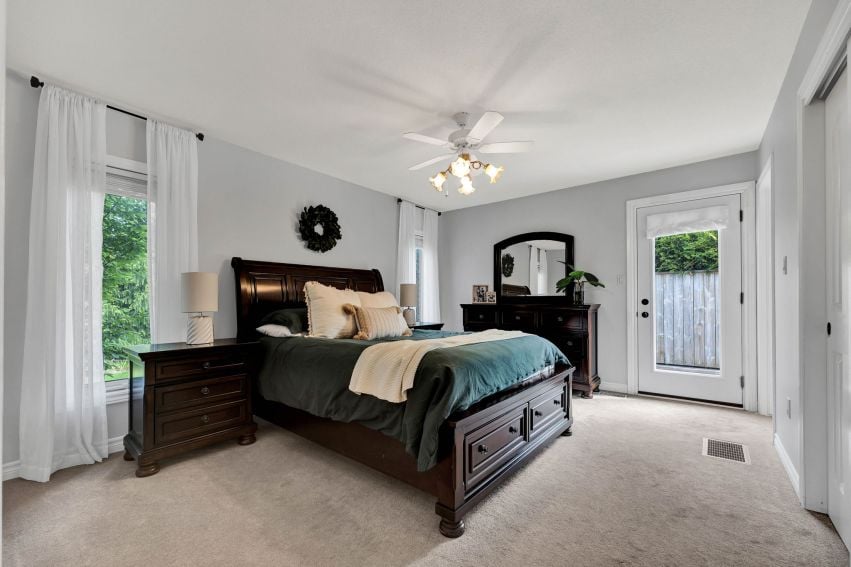 Bedroom with a dark wood bed, teal bedding, matching dressers, and tall windows.