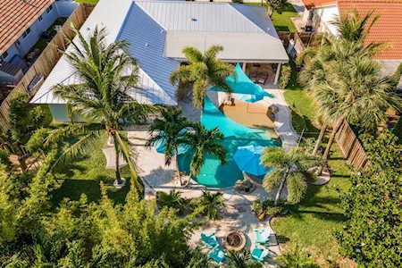 Aerial view of a home’s turquoise pool surrounded by palm trees and patio seating.