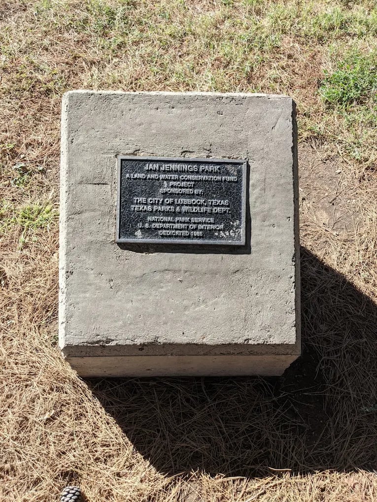 Jan Jennings Park dedication plaque mounted on a concrete monument in dry grass.