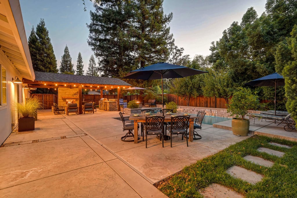 Backyard pool and patio with outdoor dining furniture and a covered seating area at dusk.