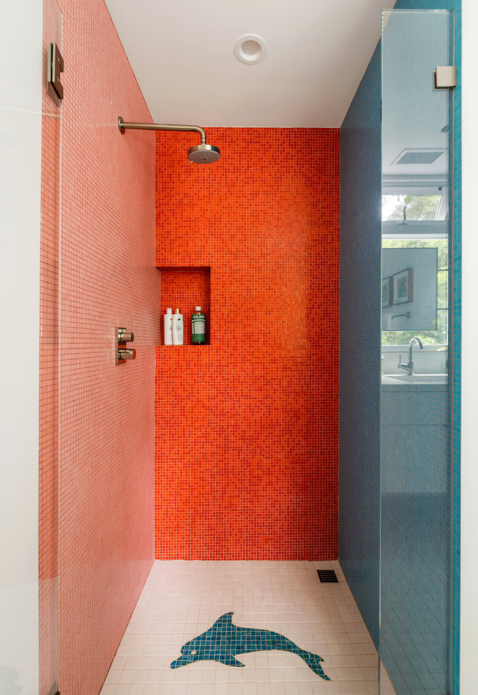 Walk-in shower with vivid red mosaic tile and a dolphin-shaped floor mosaic.