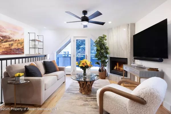 Furnished living room with a fireplace, large television, and glass doors opening to a balcony.