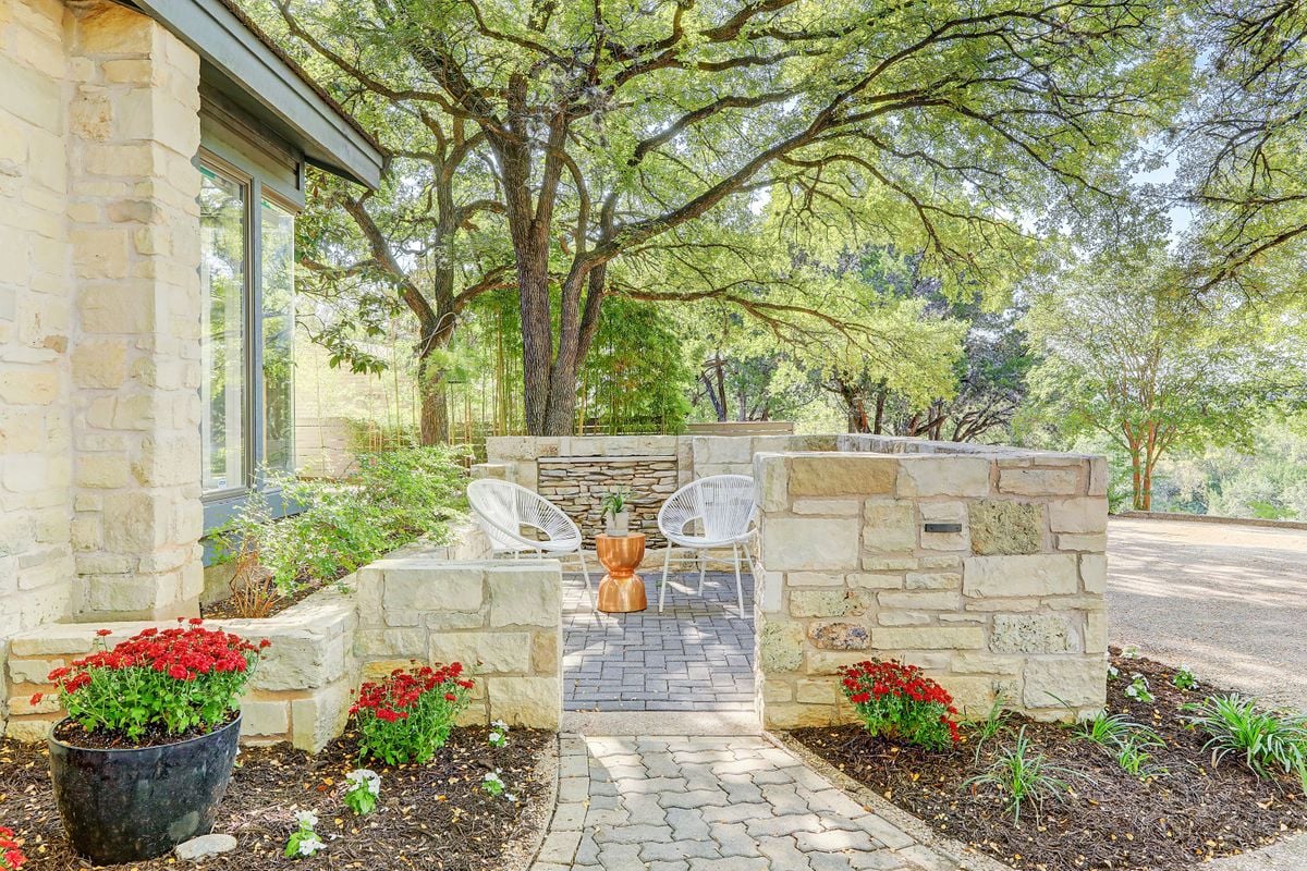 Stone-walled courtyard seating nook at 2131 Barton Hills Drive, Austin, TX 78704, with flowering potted plants along a paver walkway. Barton Hills, near South Lamar.