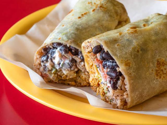 Sliced burrito with rice, beans, and salsa served on plate with foil wrap