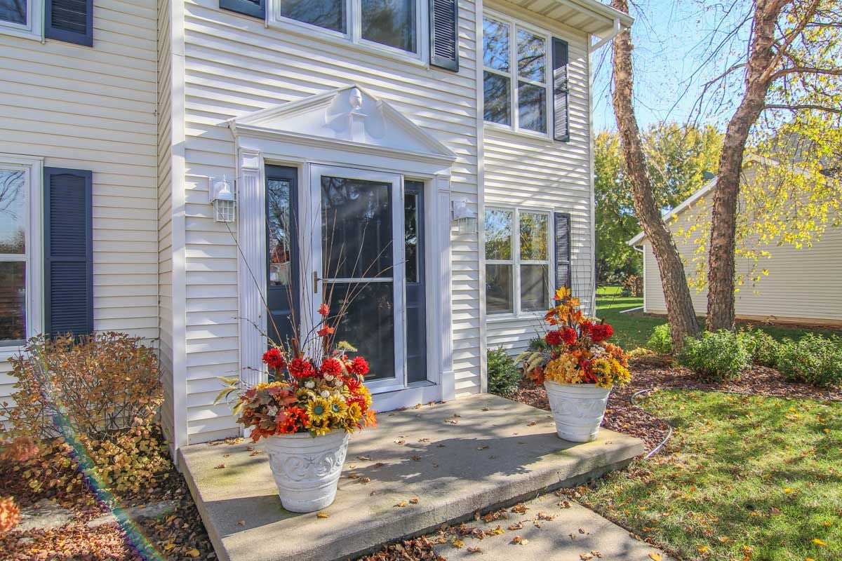 White-sided home entrance with decorative trim and autumn flower planters flanking the steps.