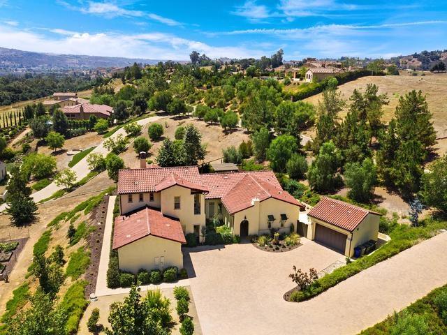 Aerial view of a tiled-roof home with a broad driveway amid rolling hills.