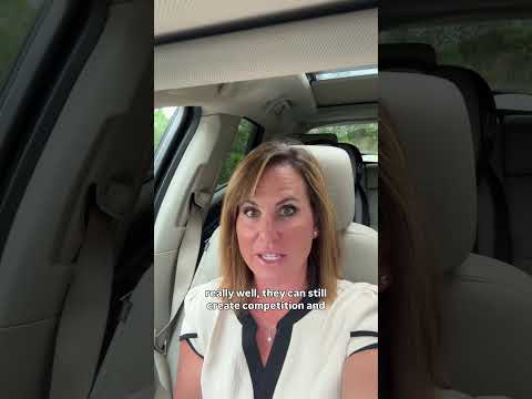 Woman speaking to camera in a car, wearing a white top with black trim.