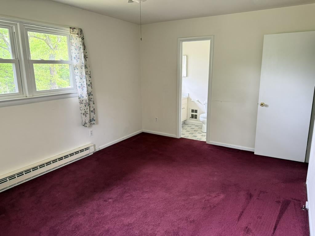 Empty bedroom with burgundy carpet, two windows, and an open doorway to a bathroom.