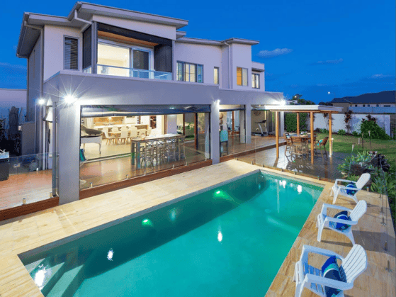 Modern two-story home with an illuminated glass patio and swimming pool at dusk.