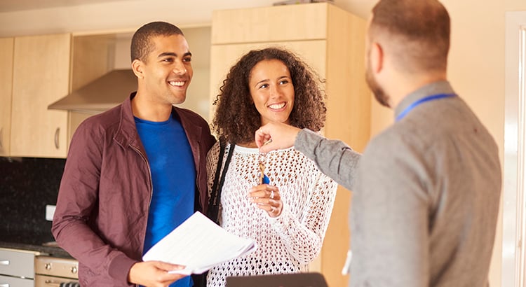 A smiling couple reviews paperwork with a real estate agent in a kitchen.