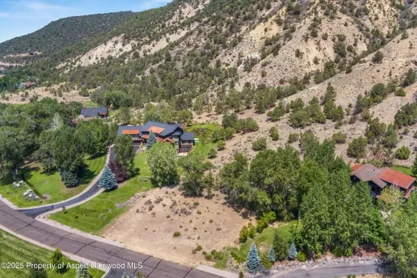 Aerial view of homes among trees below a rugged mountain hillside.
