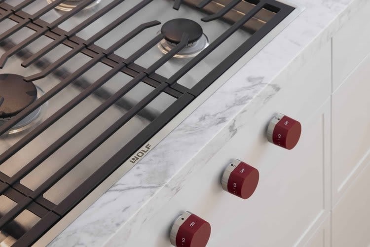 Wolf gas cooktop with black grates and red knobs set in a marble countertop.