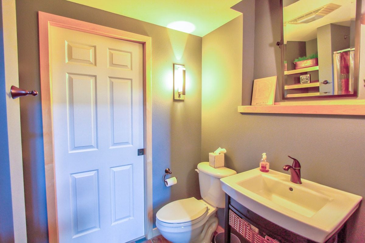 Bathroom with a white paneled door, toilet, and sink vanity beneath a mirrored medicine cabinet.