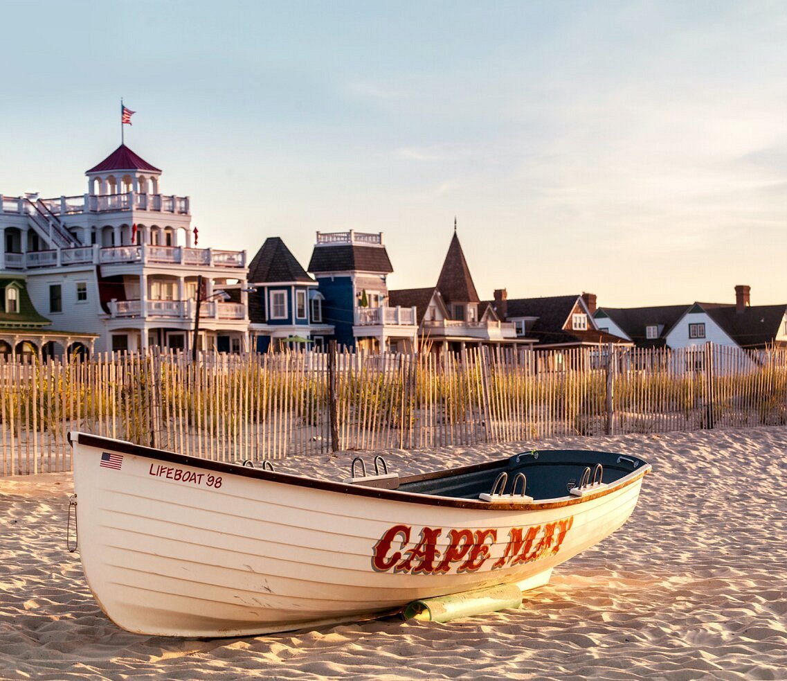 Cape May lifeboat on a sandy beach, with seaside buildings behind it.