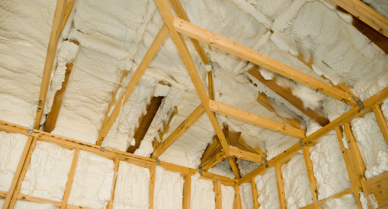 Exposed roof and wall framing filled with white spray foam insulation.