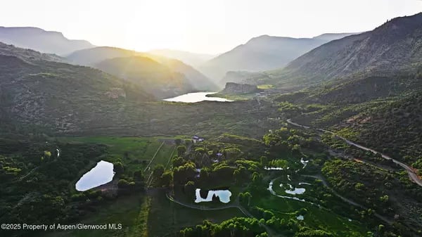 Aerial view of a green mountain valley with ponds and a winding road at sunrise.