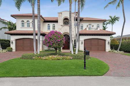 Two-story stucco home with a central arched entry, twin garages, palm trees, and a landscaped lawn.