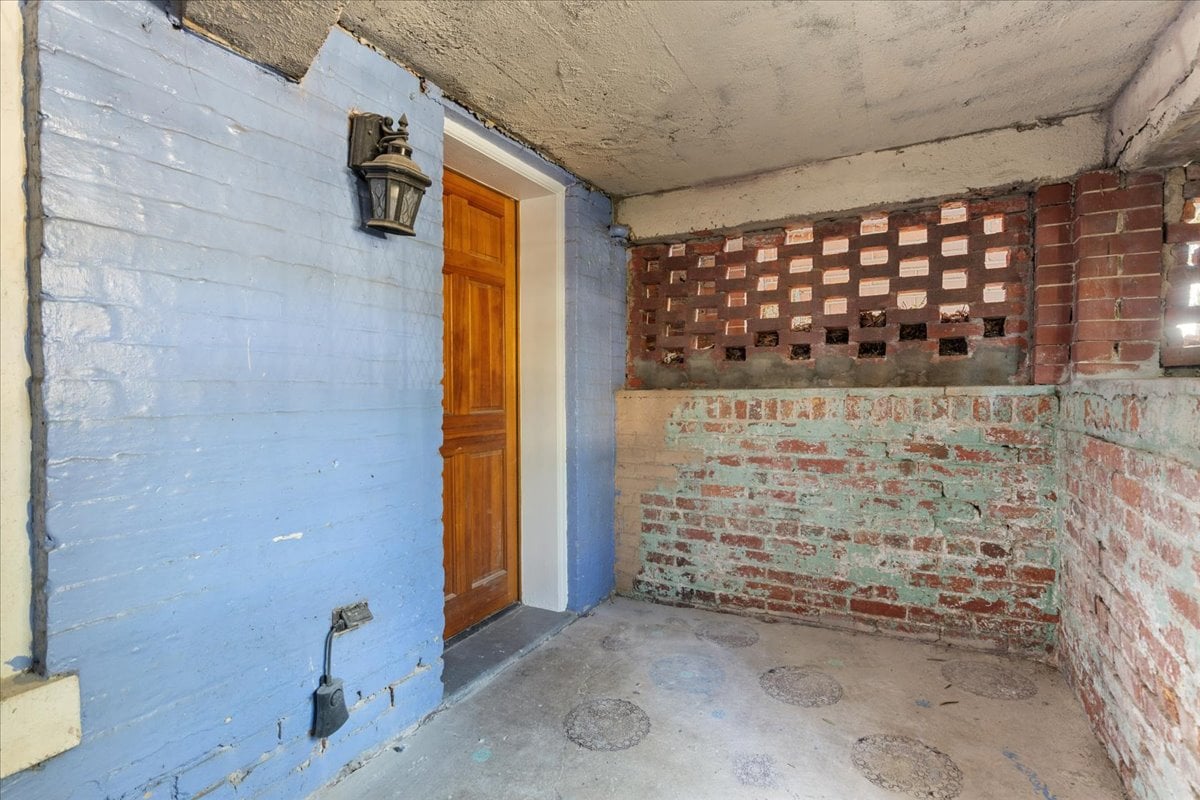 Covered brick entry with a wooden door, blue-painted wall, and concrete floor.