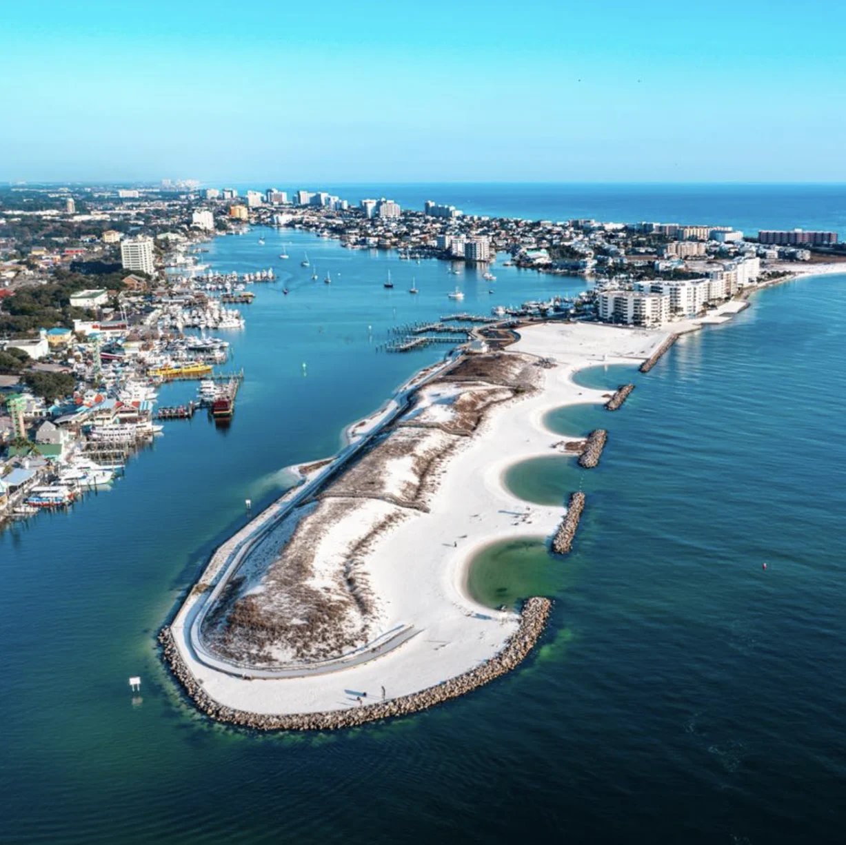 Aerial view of Destin harbor and its curved white-sand peninsula along the Gulf of Mexico.