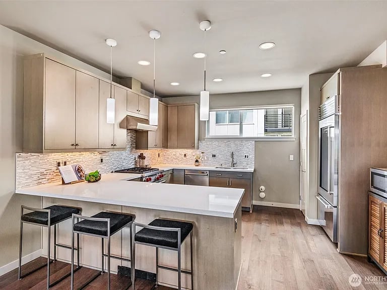 Kitchen with a large white island, three bar stools, and stainless steel appliances.