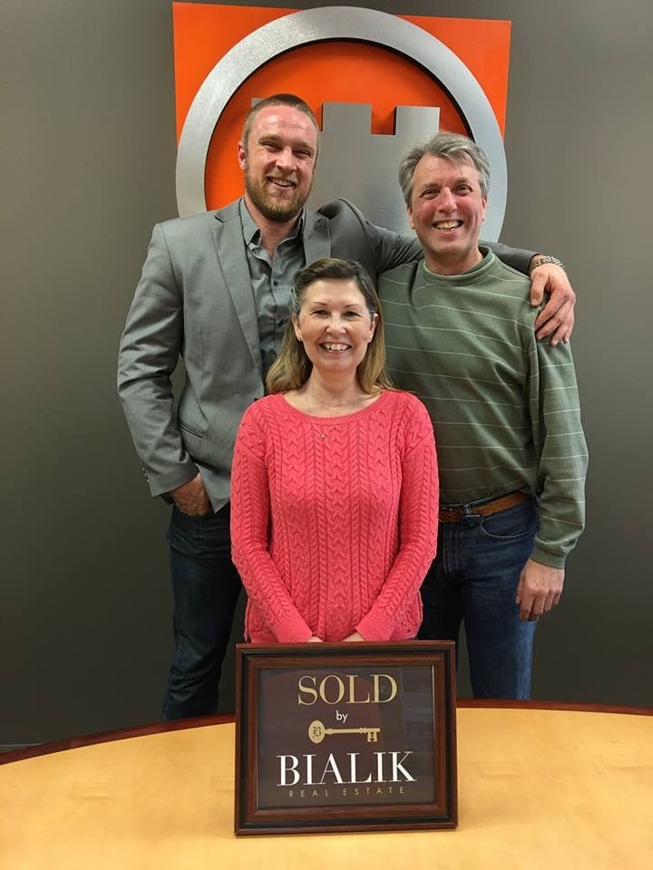 Three smiling adults pose with a SOLD by Bialik Real Estate plaque.
