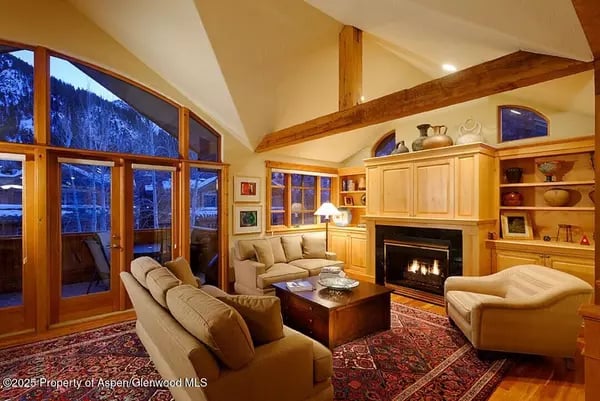 Living room with vaulted wood beams, a fireplace, and mountain views through large windows.