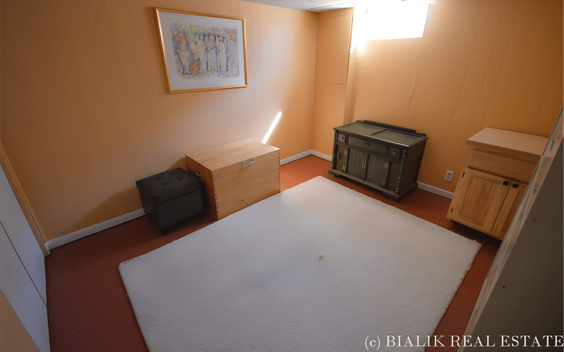 Furnished room with peach paneled walls, a large white rug, and wooden storage chests.