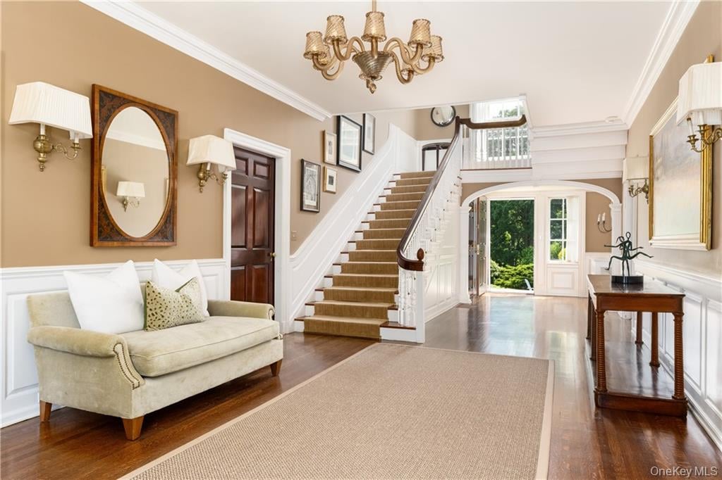 Furnished foyer with a curved staircase, beige sofa, and open entry door overlooking greenery.