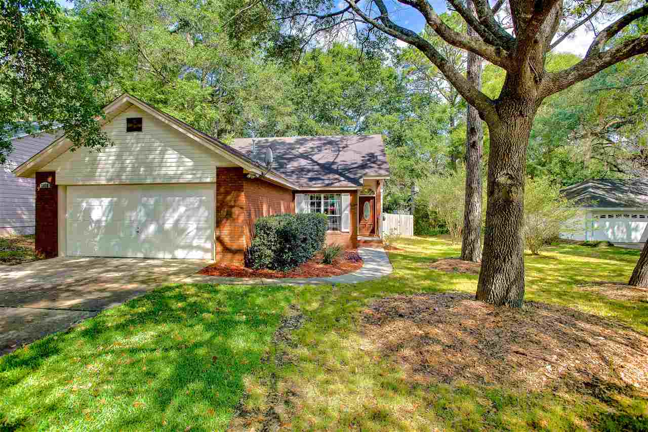 A house featuring a garage, surrounded by lush trees in the yard, creating a serene and inviting atmosphere.