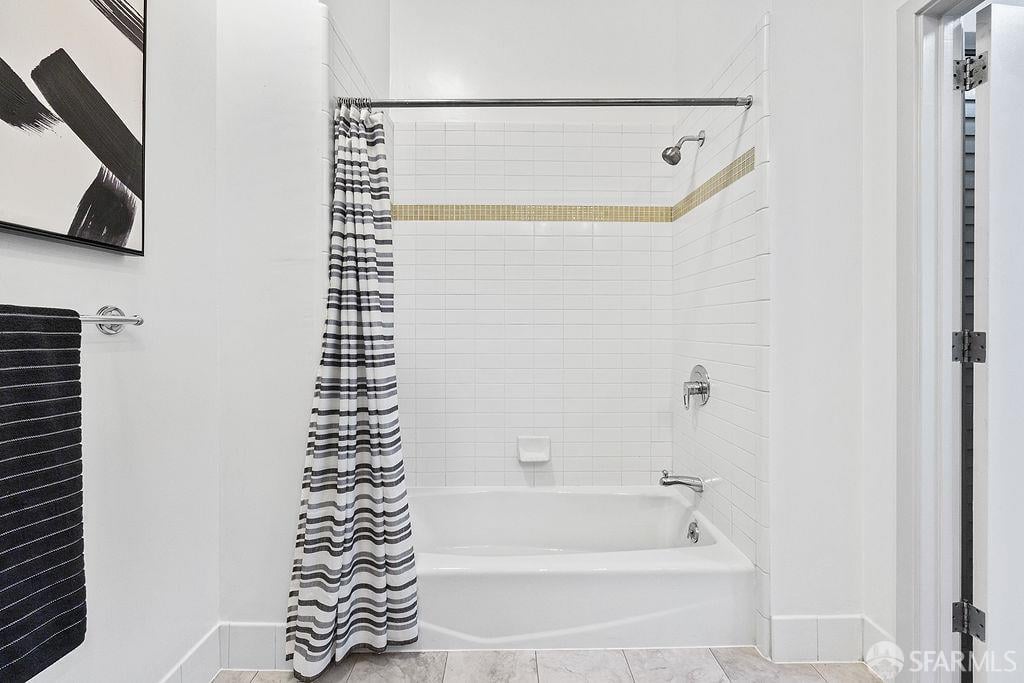 Bathroom with a white tiled tub and shower, striped curtain, and gold accent tile.