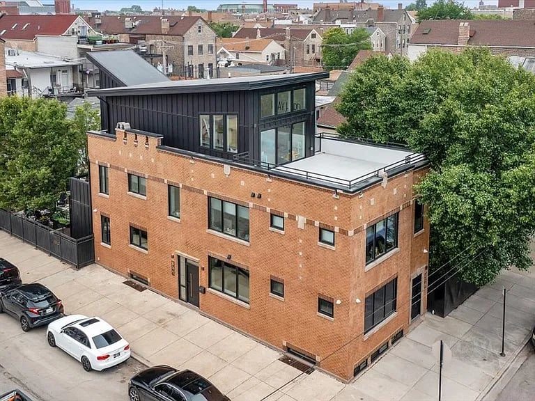 Red-brick urban building with a black upper floor and rooftop terrace, viewed from above.