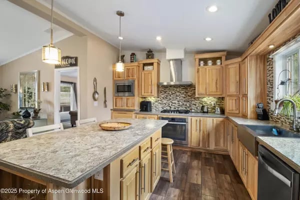 Kitchen with honey-toned wood cabinets, patterned backsplash, and a large granite island.