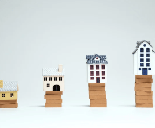 Miniature houses perched on stacks of wooden blocks at different heights.