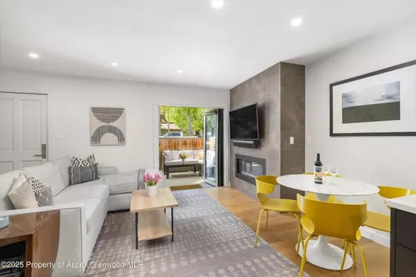 Modern living and dining room with yellow chairs, a concrete fireplace wall, and doors to a patio.