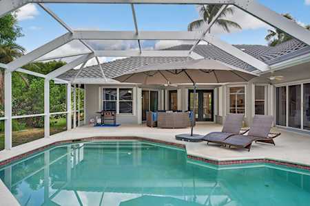 Backyard pool beneath a white screened enclosure, with lounge chairs and a covered patio.