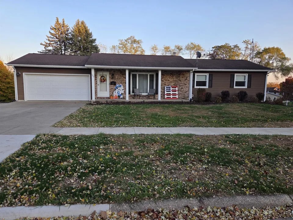 Single-story home with a wide attached garage, brick entry, and autumn leaves across the lawn.