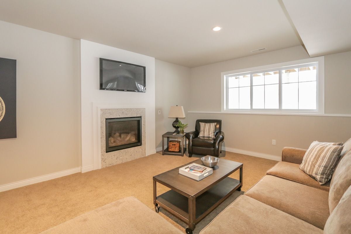 Living room with a stone-trimmed fireplace, television, leather armchair, and wide window.