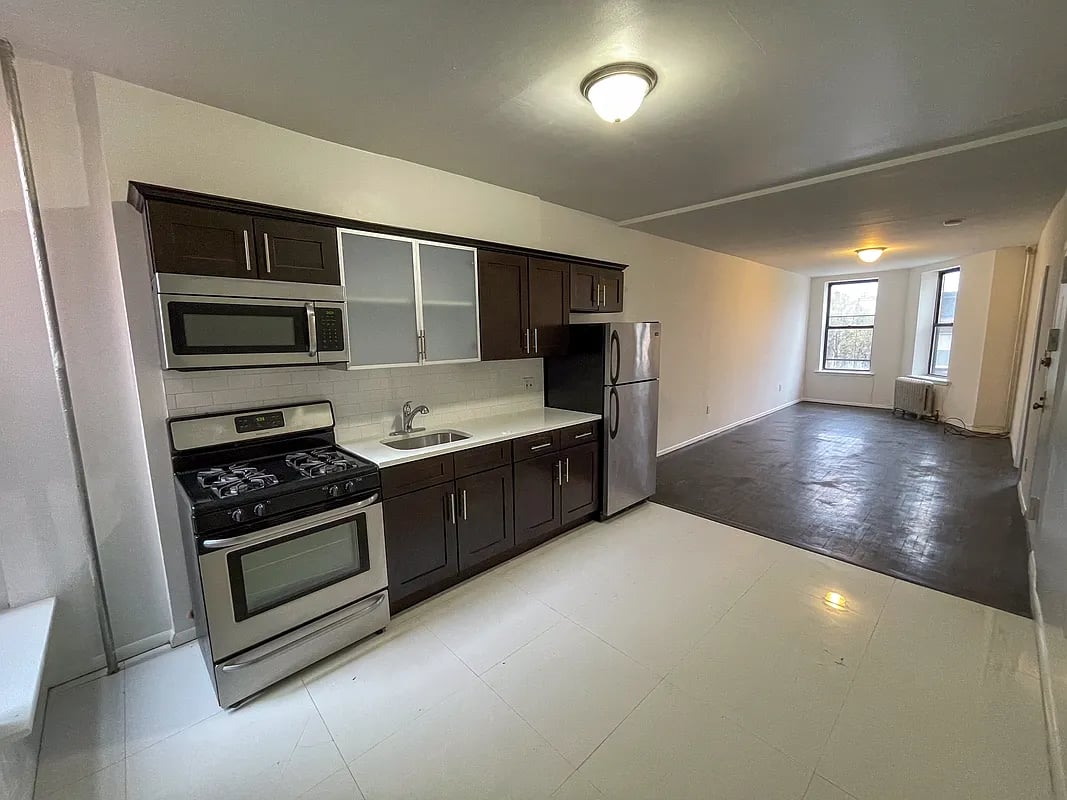 Vacant apartment kitchen with dark cabinets and stainless steel appliances opening onto a long living area.
