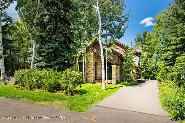 Stone-and-wood home among mature trees, with a paved driveway and landscaped lawn.