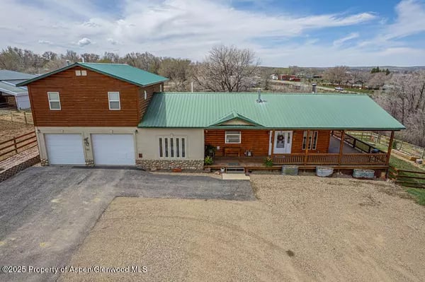 Two-story brown home with green metal roofs, attached garages, and a long covered porch.