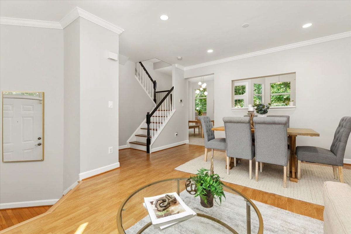 Dining and living area with a hardwood floor, gray dining chairs, and a staircase beside the entryway.