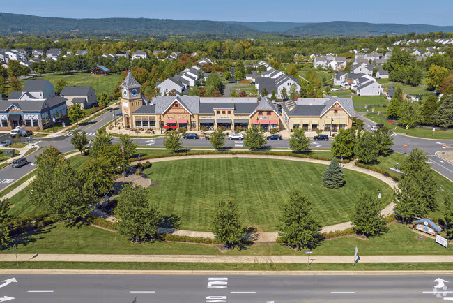Aerial view of a shopping center with a clock tower and circular lawn beside a main road.