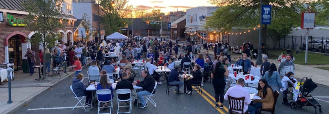 Crowds dine at outdoor tables filling a downtown street at dusk.