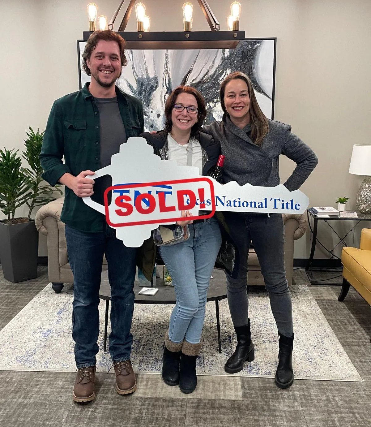 Three adults pose with an oversized key-shaped sign stamped SOLD.