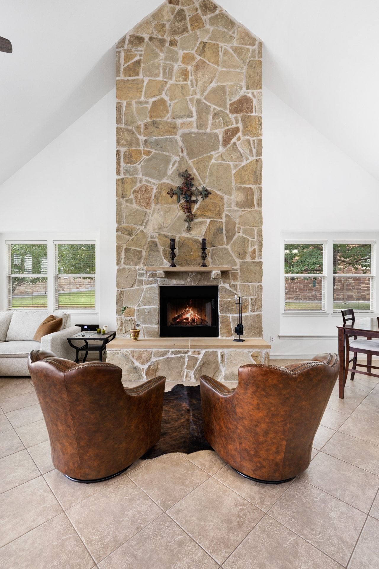 Living room with a tall stone fireplace, lit fire, and two brown leather armchairs.