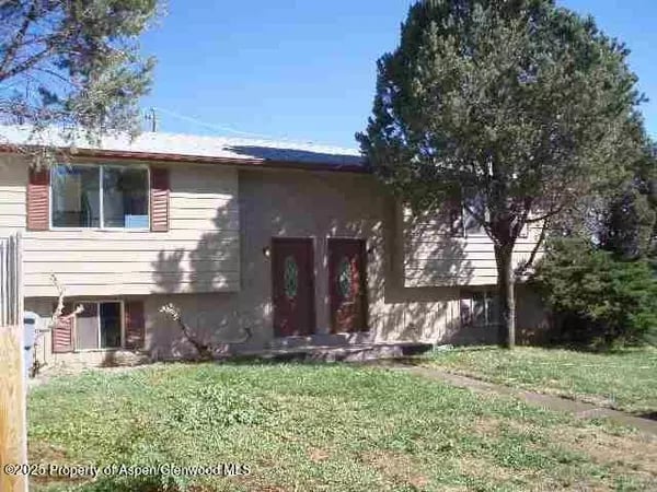 Split-level home with two red entry doors, shuttered windows, and mature trees.