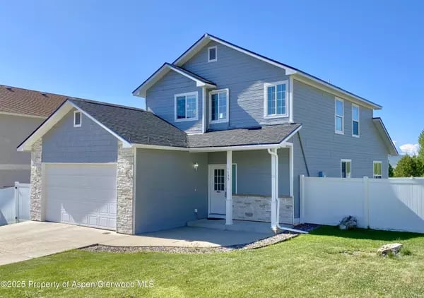 Two-story gray house with an attached garage, white privacy fence, and green lawn.