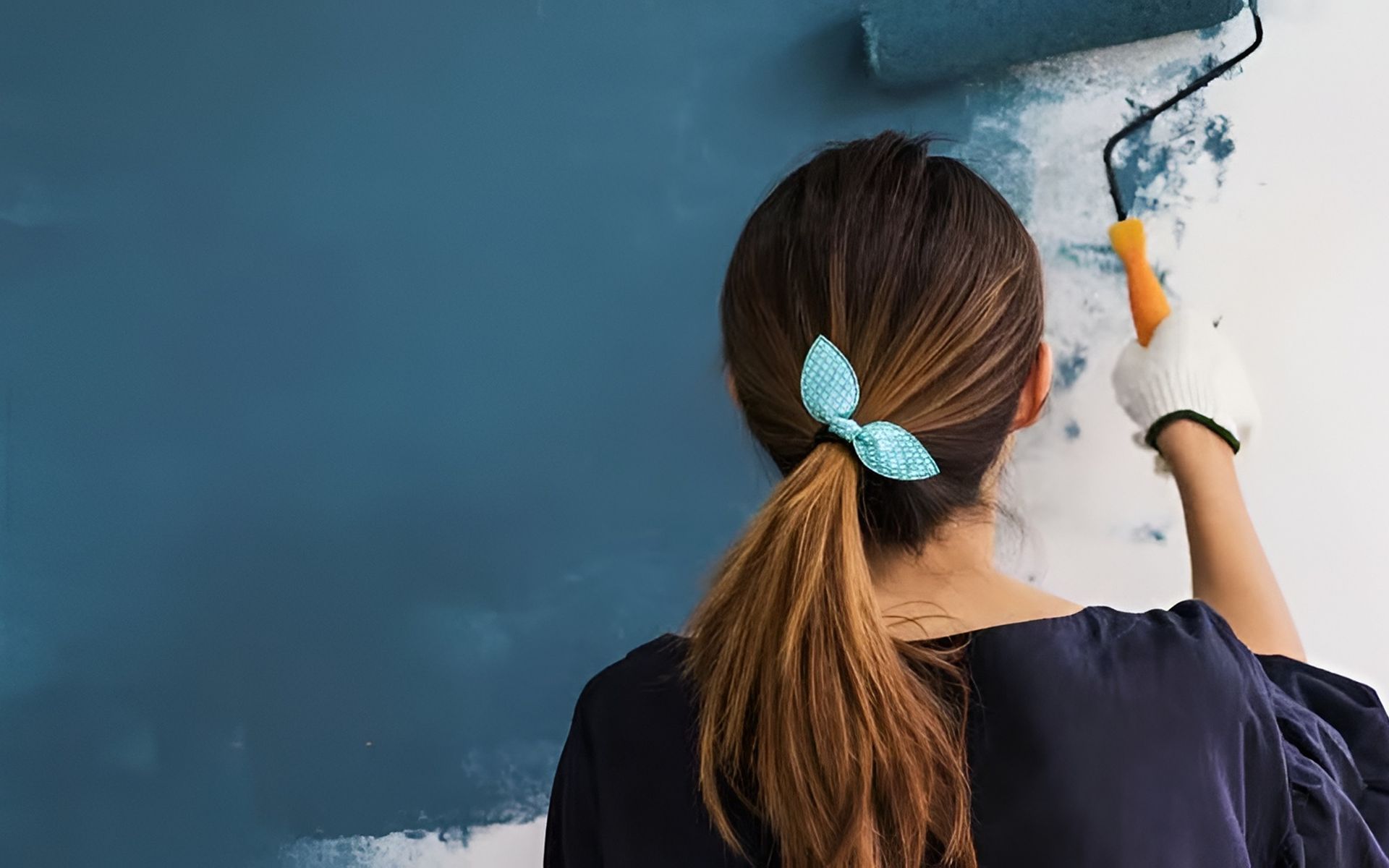 A woman paints a blue interior wall with a roller.