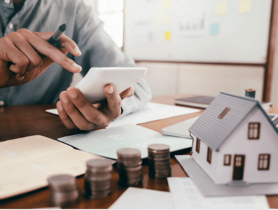 Person reviewing property investment figures beside coins and a model house.