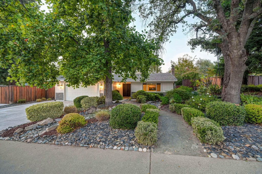 Single-story home with an attached garage, mature trees, and a landscaped front garden.